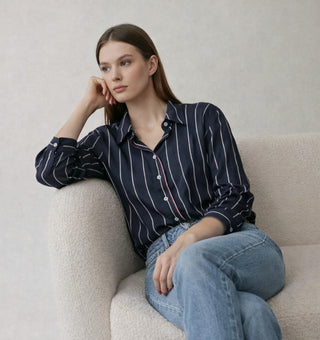 Woman in a navy pinstripe button-down shirt and jeans, seated in a cream armchair