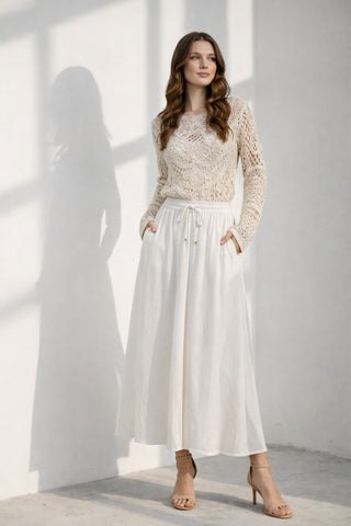 Woman in a cream crochet top and white maxi skirt standing in sunlight
